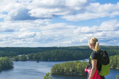 Nainen katsoo korkealta kalliolta suomalaista järvimaisemaa.